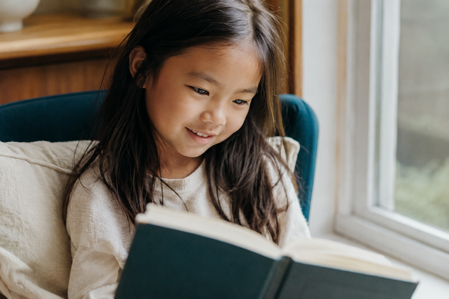 A young girl reading happily by a bright window